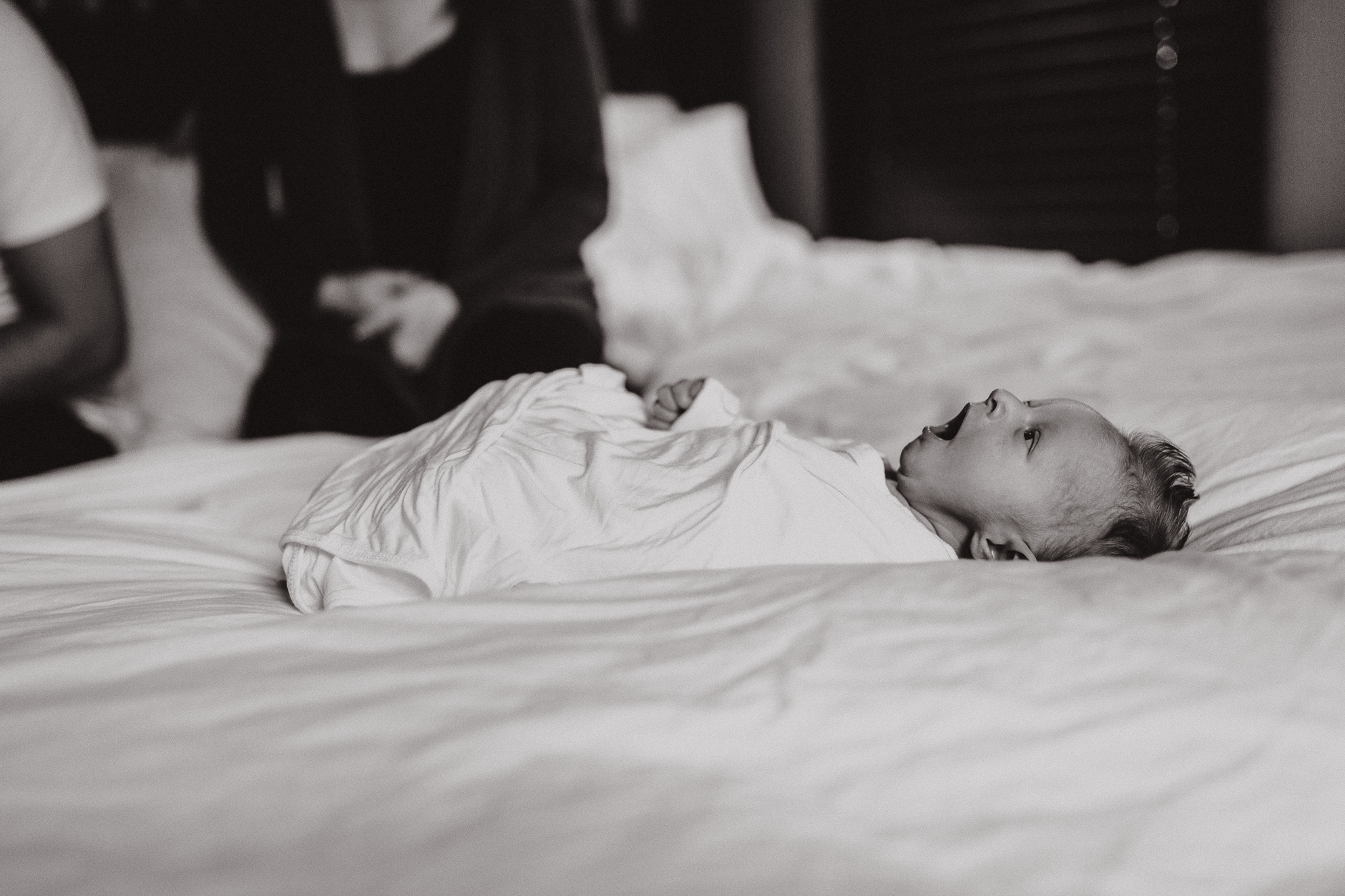 Baby boy swaddled and yawning on the bed.